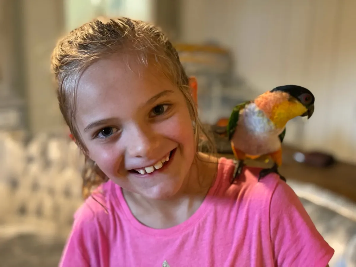 a little girl smiling at the camera with a bird on her shoulders